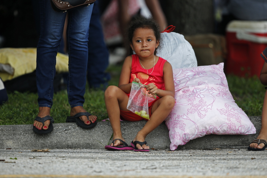 Yameleth Georges, 5, sits on a curb as her family lines up with evacuees to enter the Germain Arena, which is being used as a shelter, in advance of Hurricane Irma, in Estero, Fla.