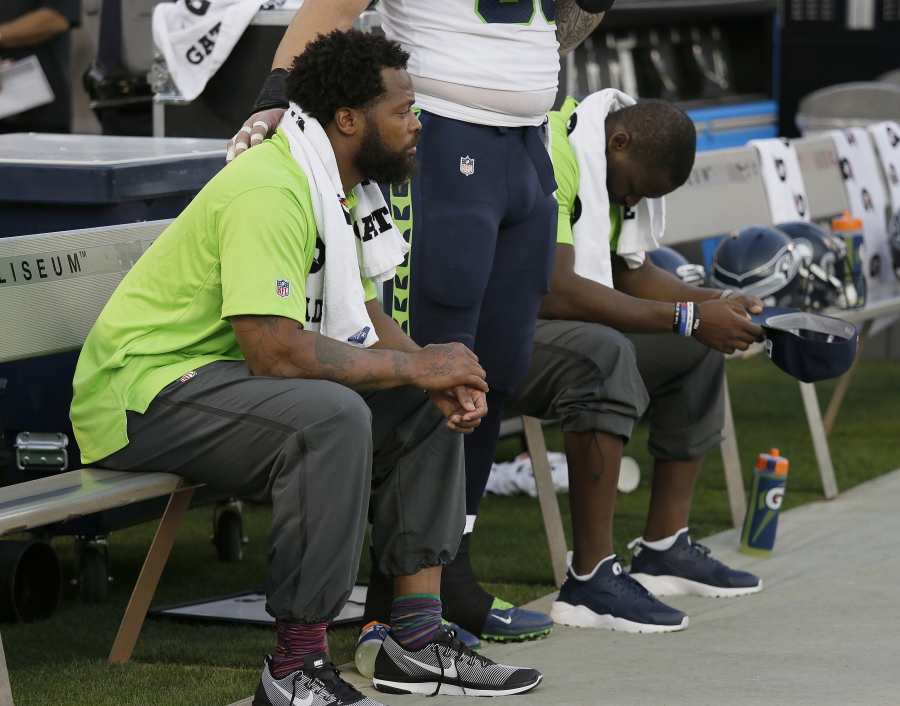 Seattle Seahawks defensive end Michael Bennett, left, sits during the playing of the national anthem next to Justin Britt, center, and another teammate before an NFL preseason football game between the Raiders and the Seattle Seahawks in Oakland, Calif. Bennett is accusing Las Vegas police of racially motivated excessive force when he says he was detained at gunpoint on Aug. 27, 2017, handcuffed and later released without charges following a report that gunshots were heard at a casino hotel.