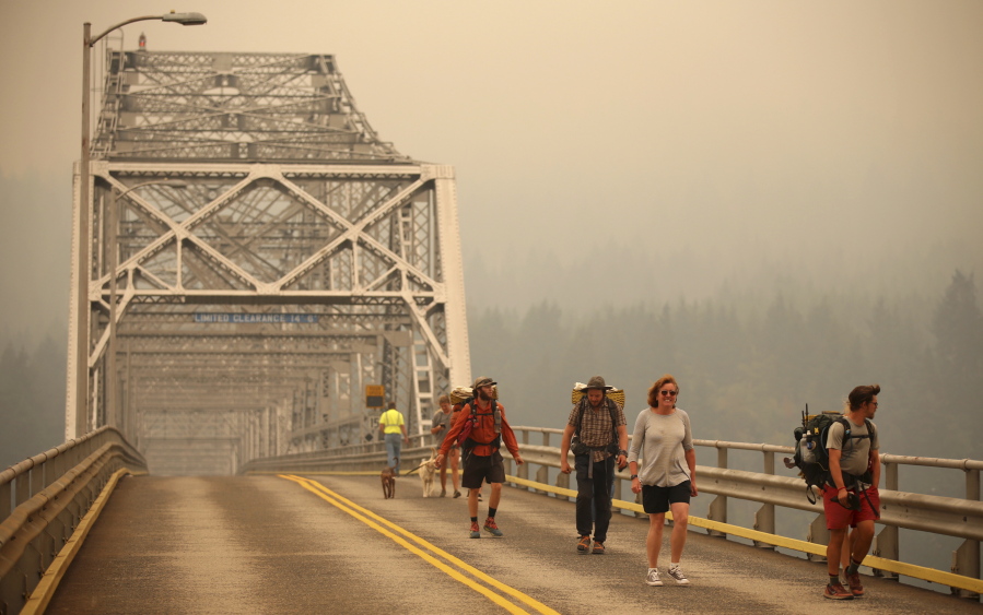 Pedestrians walk across the Bridge of the Gods, which spans the Columbia River, as smoke from the Eagle Creek wildfire obscures the Oregon hills in the background. Randy L.