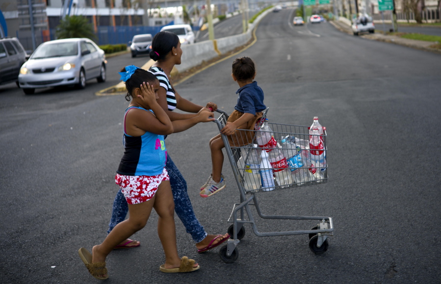 A resident pushes a shopping cart full of recycled bottles filled with water she collected from a water distribution center, in Bayamon, Puerto Rico, Thursday, Sept. 28, 2017. The aftermath of the powerful storm has resulted in a near-total shutdown of the U.S. territory’s economy that could last for weeks and has many people running seriously low on cash and worrying that it will become even harder to survive on this storm-ravaged island.