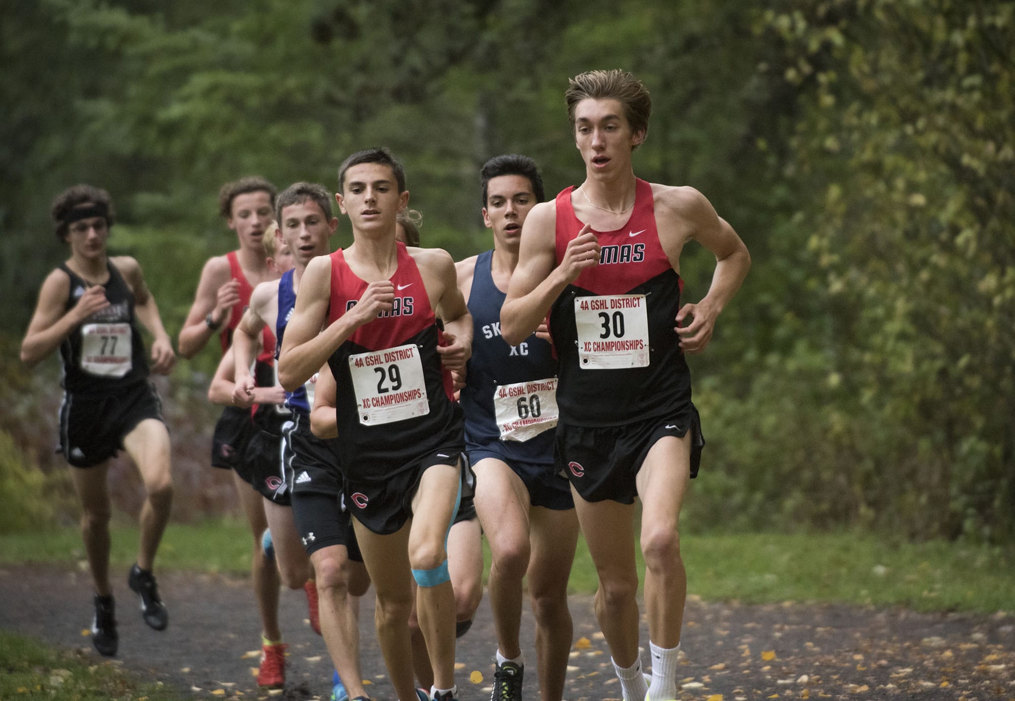 Camas’ Jackson Lyne (29), left, Skyview’s Bruce Erickson (60) and Camas’ Daniel Maton (30) race down trail at Lewisville Park in Battle Ground, Wednesday October 18, 2017, during the boy’s 4A district cross country championships.