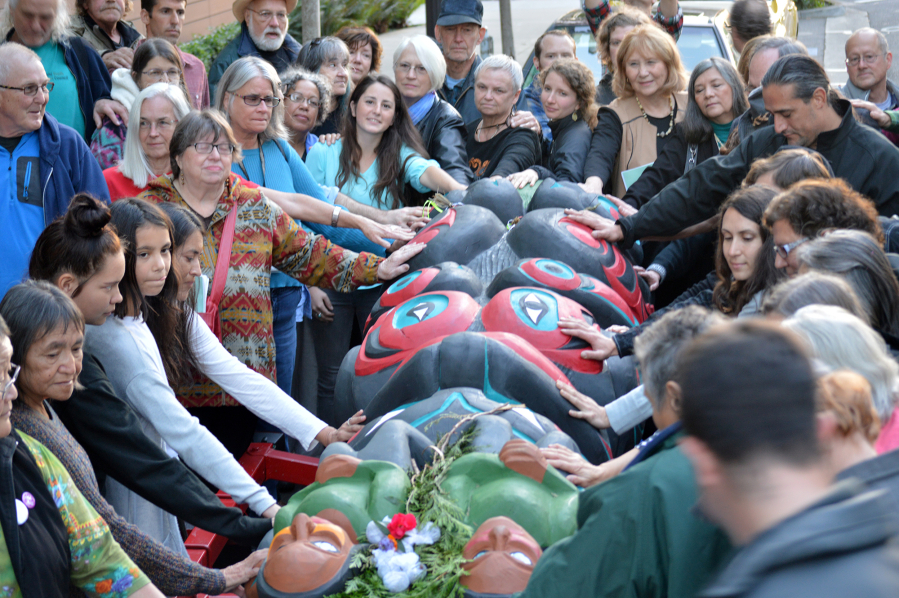 A crowd lays their hands on a totem pole bound for the Carnegie Museum of Natural History Monday evening.