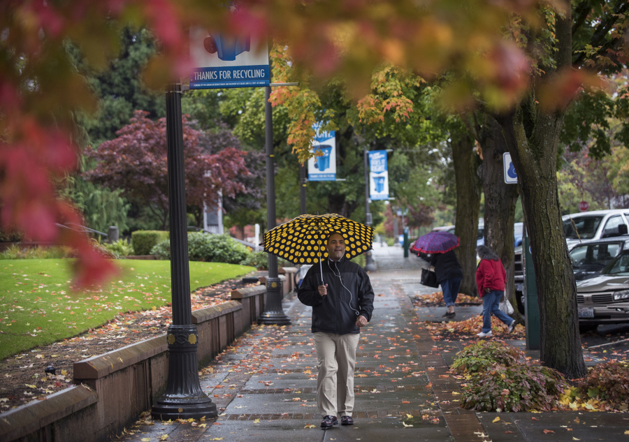 Jose Alvarez walks through rain and falling leaves by the Clark County Courthouse on Franklin Street in Vancouver on Thursday. More rain and wind is expected through the weekend.