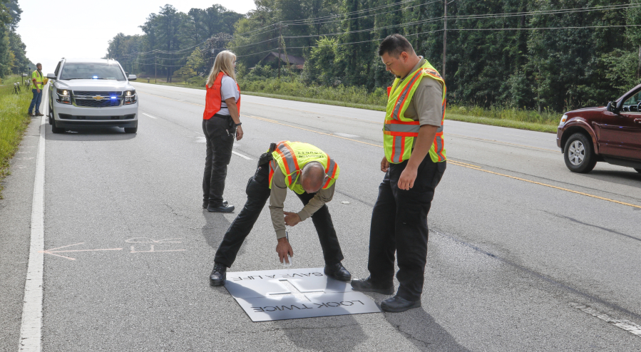 Lexington County, S.C., Coroner Grey Gain, center, paints a cross in September on Route 378 in South Carolina where a pedestrian was killed.