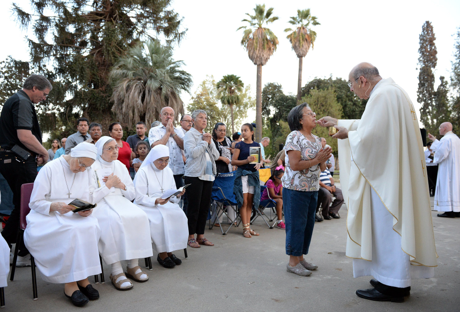 Bishop Armando X. Ochoa of the Roman Catholic Diocese of Fresno, Calif., gives communion to participants during a mass at Kearney Park as part of the Roman Catholic Diocese of Fresno’s 50th anniversary conducted through their mobile chapel .