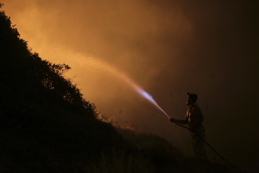 A volunteers uses a water hose to fight a wild fire raging near houses in the outskirts of Obidos, Portugal, in the early hours of Monday.