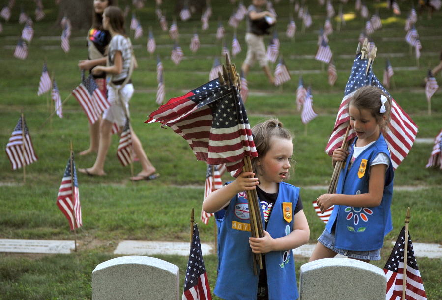 FILE - In this May 23, 2012 file photo, Natalie Benson, 5, and Holly Sweezer, 6, carry extra flags as Boy and Girl Scouts place flags on each of the 5,000 headstones at the Grand Rapids Veterans State Cemetery in Grand Rapids, Mich. The Wednesday, Oct. 11, 2017 Boy Scouts of America announcement to admit girls throughout its ranks will transform what has been a mostly cordial relationship between the two iconic youth groups since the Girl Scouts of the USA was founded in 1912, two years after the Boy Scouts.