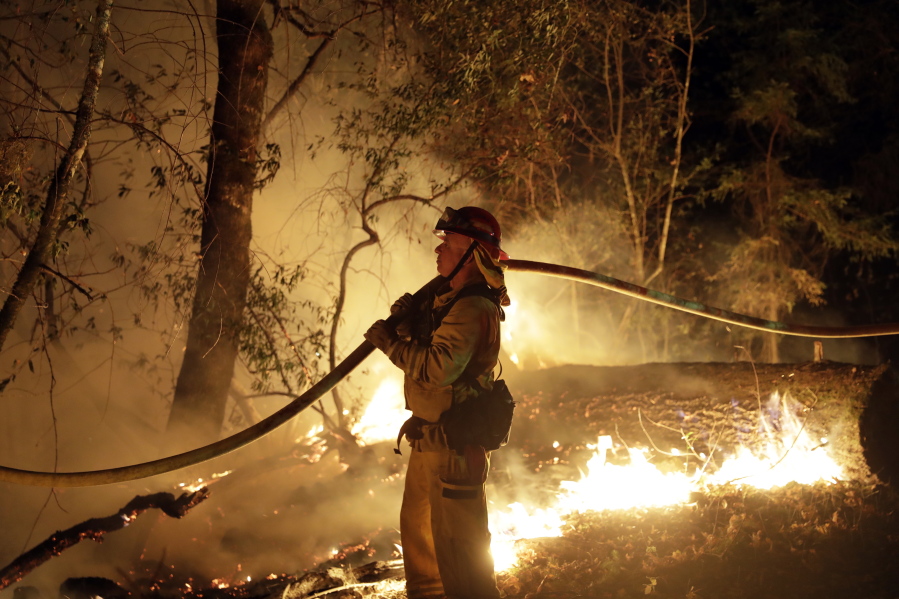 A firefighter holds a water hose while fighting a wildfire Saturday in Santa Rosa, Calif.