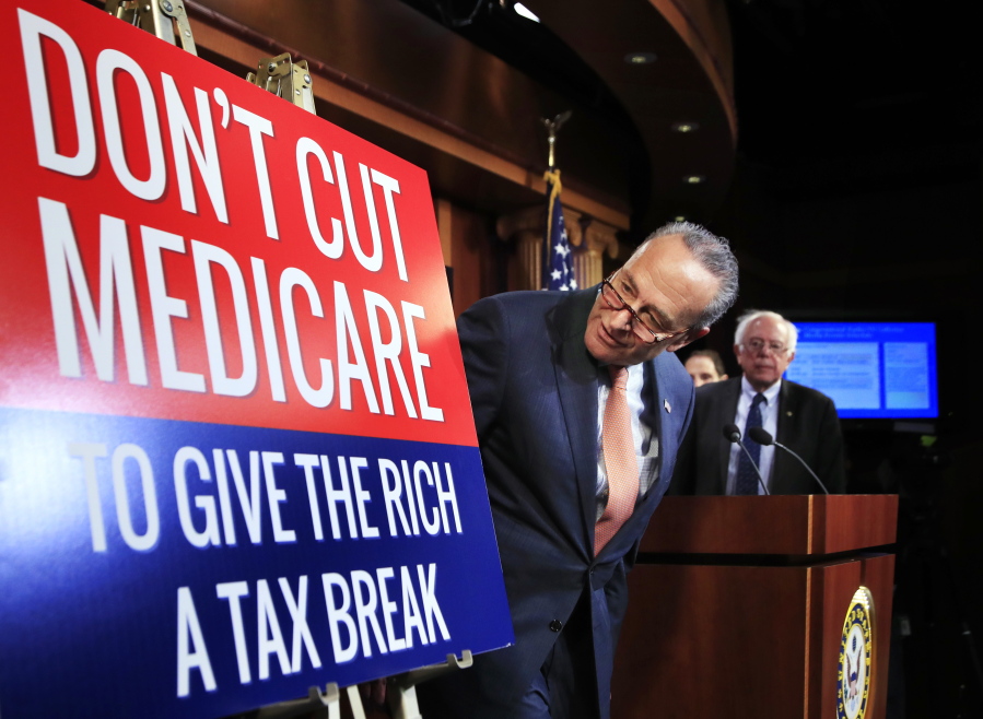 Senate Minority Leader Chuck Schumer of New York, followed by Sen. Bernie Sanders, I-Vt., look at a poster at the start of a news conference on Capitol Hill in Washington, Wednesday, October 4, 2017, urging Republicans to abandon cuts to Medicare and Medicaid.