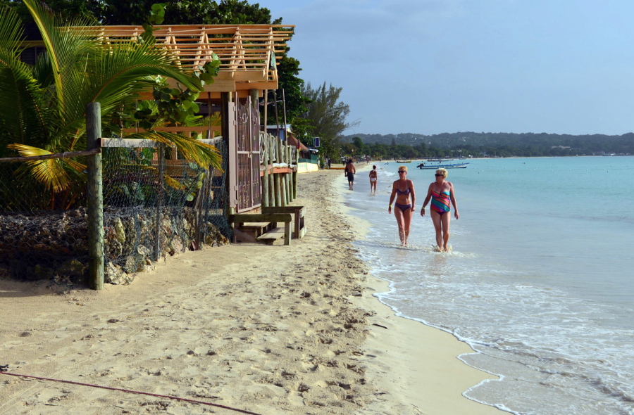 FILE - In this Sept. 14, 2014, file photo, sunbathers walk along a badly eroding patch of resort-lined crescent beach in Negril in western Jamaica. While some islands in the Caribbean were hard-hit by this season’s hurricanes, others were relatively unscathed and are open for business as usual.