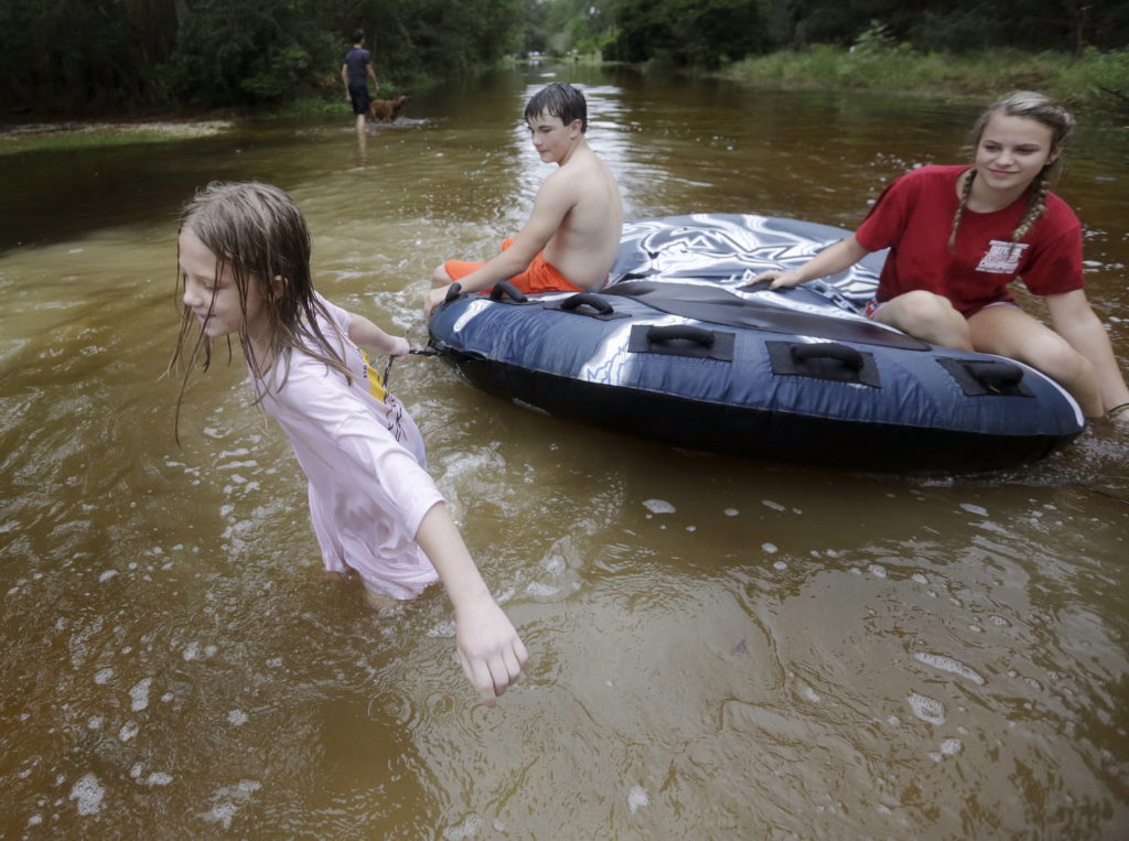 Crimson Peters, 7, left, Tracy Neilsen, 13, center, and Macee Nelson, 15, ride in an inner tube down a flooded street after Hurricane Nate, Sunday, Oct. 8, 2017, in Coden, Ala.