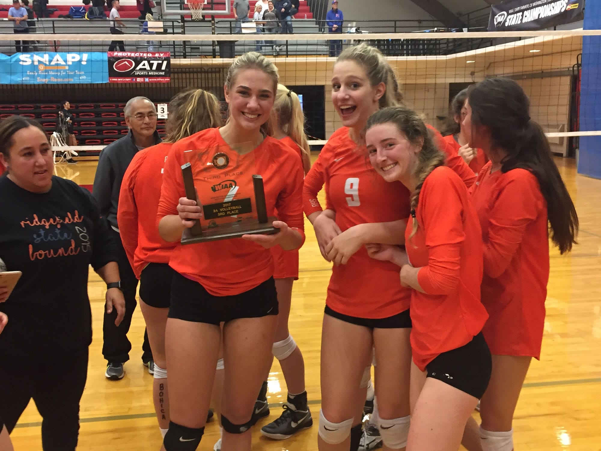 Ridgefield volleyball players, from left, Anika Nicoll, Kameryn Reynolds and Haley Paul celebrate with the third-place trophy at the Class 2A state tournament Saturday in Lacey.