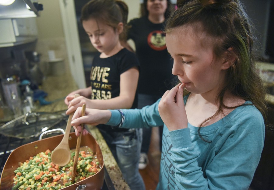 Maddie Wallingford, 9, right, tries a piece of frozen corn while making shepherd’s pie with her sister, 6-year-old Hazel, and mom, Mari, at their Vancouver home Tuesday evening. Maddie used to be an extremely picky eater until she went through Innovative Services NW’s food therapy program.