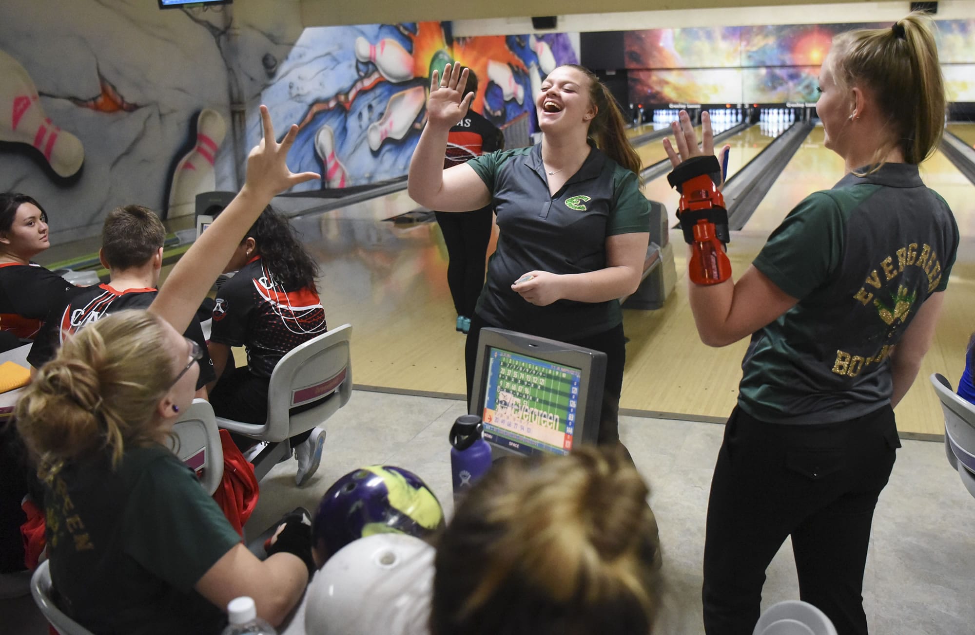 Evergreen junior Kerissa Andersen, center, reaches out to high-five bowling teammates Dakota O’Neil, left, and Alexis Henderson, right, after making a strike during the season opening jamboree at Crosley Lanes in Vancouver, Thursday November 9, 2017.