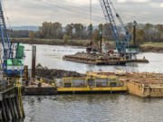 Legacy contamination from the former Reynolds aluminum plant is being cleaned up now just off the dike at Millennium Bulk Terminals Longview site on the Columbia River. Work started late last month dredging up a two-foot-thick layer of normal, silted river bottom and the two-foot-thick layer of contaminated soils which the silt covered. Wednesday, a barge-mounted crane was refilling the hole with certified clean sand. Work will continue today. The contaminated area is located just downriver from Millennium’s dock, and near where the company discharges all the treated surface water collected on the site back into the Columbia. The yellow-sided barge in the foreground contains some of the contaminated soil dredged earlier.