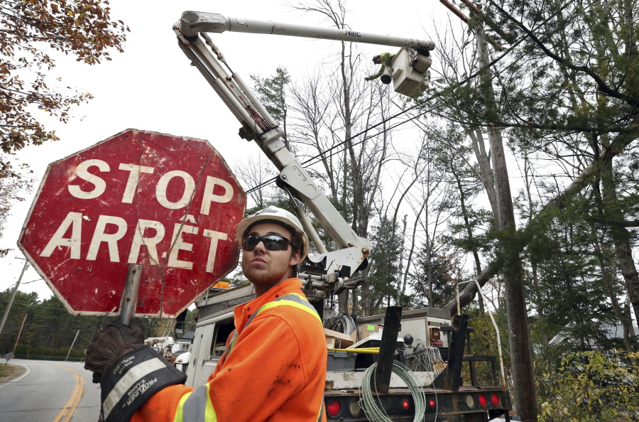 Canadian lineman Noah Clowater holds a bilingual stop sign while directing traffic while his coworkers restore power Wednesday in Yarmouth, Maine. The New Brunswick, Canada, crew were among the hundreds of line and tree workers from as far away as Illinois, Kentucky, Ohio and West Virginia that have come to Maine following Monday’s storm that knocked out power to nearly two-thirds of the state. (AP Photo/Robert F.