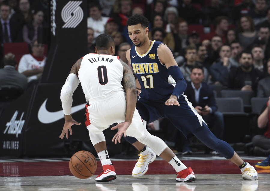 Portland Trail Blazers guard Damian Lillard dribbles behind his back to get around Denver Nuggets guard Jamal Murray during the first half of an NBA basketball game in Portland, Ore., Monday, Nov. 13, 2017.