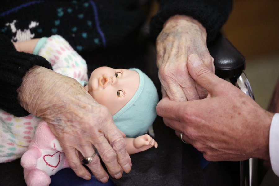 A son, at right, holds his mother’s hand at her nursing home in Michigan.