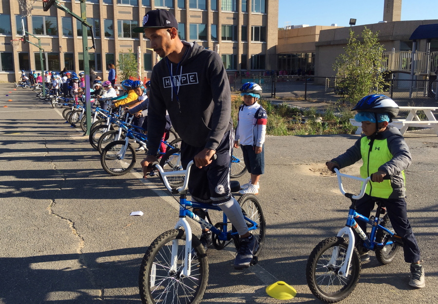 In this Oct. 3, 2017, photo, second-graders learn to ride bikes on the school yard from physical education teacher Terrance Chavis at Seaton Elementary School in Washington. At a time when elementary and high schools are all about getting students ready for college or jobs, physical education teachers are being urged to look beyond graduation, too, to make lifelong movers out of even the least competitive kids.