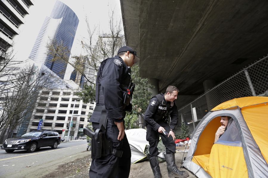 Seattle police officers Wes Phillips, left, and Tori Newborn talk March 23, 2017 with Corvin Dobschutz as the homeless man sits in his tent below a freeway and next to downtown Seattle.