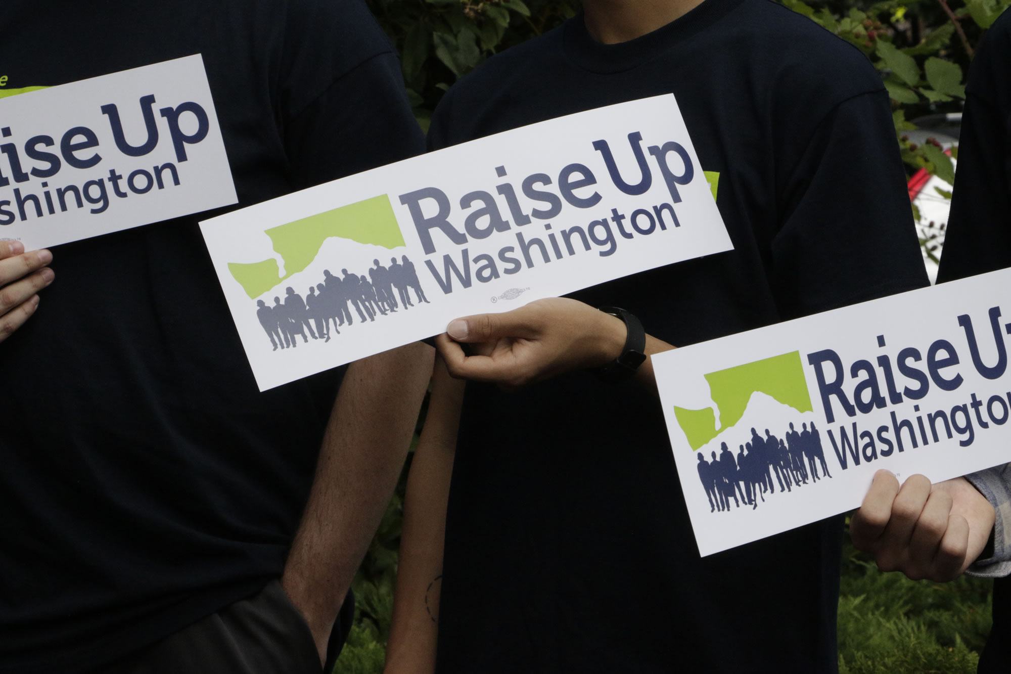 Supporters of raising the state minimum wage hold signs at a news conference, in 2016 in Olympia. Initiative 1433, approved by votes, incrementally increases the state's rate over the next four years to $13.50 an hour and to provide paid sick leave to employees who don't currently have it.