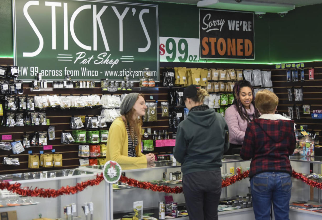 Budtender Sarah Rosdahl, left, and Kayzla Worlitz, an assistant manager at Sticky’s Pot Shop, help customers pick out products on Wednesday. The shop remains open, despite a county ban, while the law is contested in the courts.