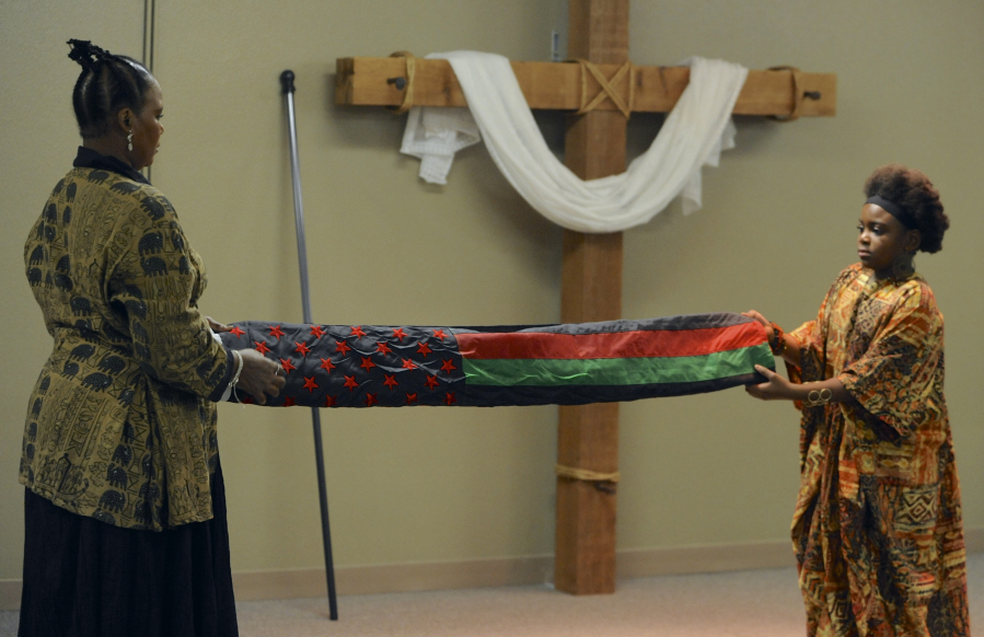 Marcella Leonard, left, and Marianna Leonard fold the African-American flag at the beginning of the Kwanzaa Celebration at the New Directions Community Church in Vancouver on Saturday.