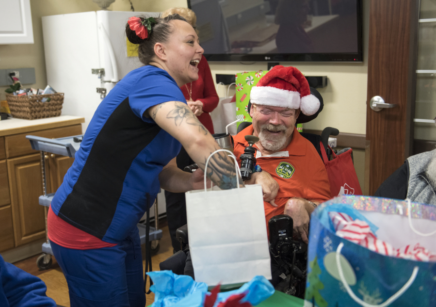 Prestige Care and Rehabilitation in Camas nursing assistant Sarah Richmond of Vancouver helps resident Ronald Hoffman open his gift delivered by the local Home Instead Senior Care Vancouver chapter.