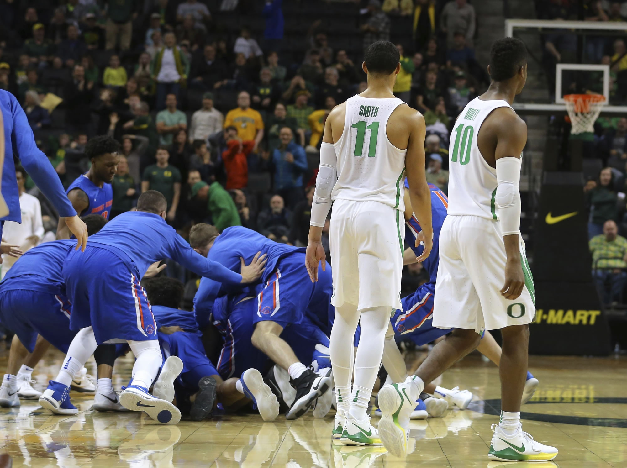 Oregon's Keith Smith (11) and Victor Bailey Jr. (10) leave the court as Boise State players pile on Lexus Williams after his 40-foot buzzer-beater defeated Oregon 73-70, snapping the Ducks' 46-game home winning streak, in Eugene, Ore., Friday, Dec. 1, 2017.