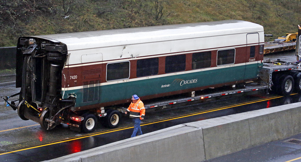 A worker walks along a damaged train car atop a flat bed trailer taken from the scene of Monday's fatal Amtrak train crash onto Interstate 5 Tuesday, Dec. 19, 2017, in DuPont, Wash.  The Amtrak train that plunged off an overpass south of Seattle was hurtling 50 mph over the speed limit when it jumped the track, federal investigators said.
