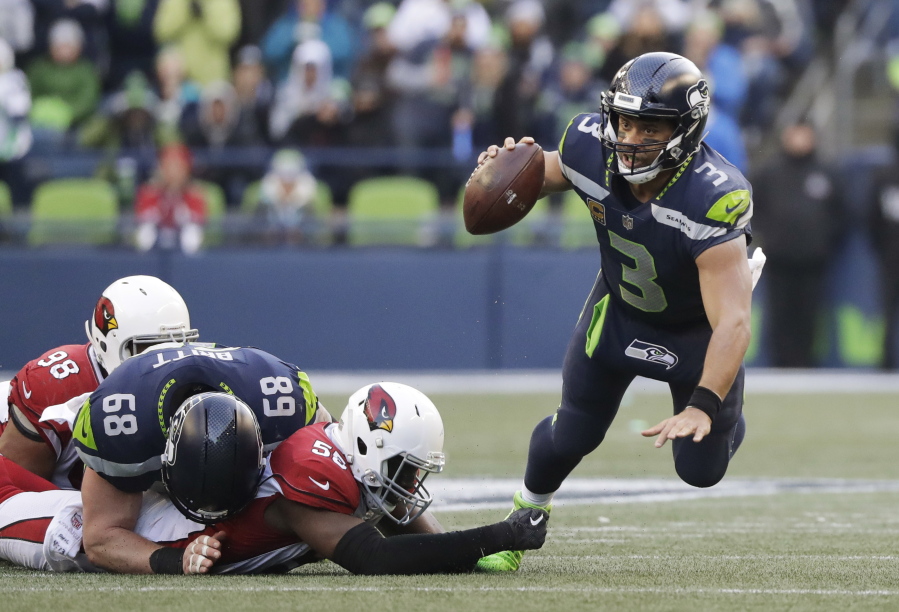 Seattle Seahawks quarterback Russell Wilson, right, is tripped by Arizona Cardinals outside linebacker Chandler Jones, second from right, in the second half of an NFL football game, Sunday, Dec. 31, 2017, in Seattle.