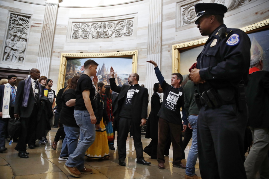With shirts saying “fight poverty not the poor,” people with the “Poor People’s Campaign” gesture the group to remain quiet as the group leaves the Capitol Rotunda on Monday after praying in an act of civil disobedience in protest of the GOP tax overhaul in Washington.