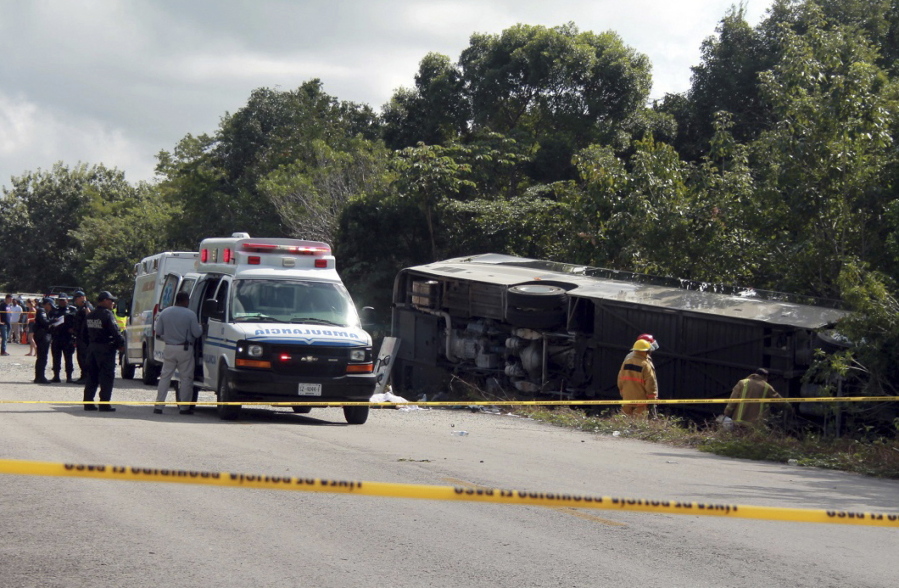 An ambulance sits next to an overturned bus Tuesday in Mahahual, Mexico. The bus, carrying cruise ship passengers on a shore excursion to the Mayan ruins at Chacchoben, flipped over on a highway, killing 12 people and injuring 20.