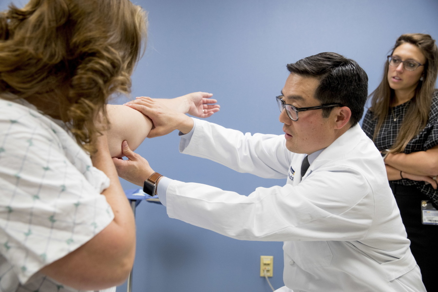 In this Sept. 21, 2017, photo, Dr. David Song accompanied by nurse Christina Barra, right, examines Susan Wolfe-Tank’s arm for signs of lymphedema during a post-surgery checkup at MedStar Georgetown University Hospital in Washington. Wolfe-Tank underwent lymph node transfer surgery to ease the severe swelling, a lasting side effect of her breast cancer treatment.