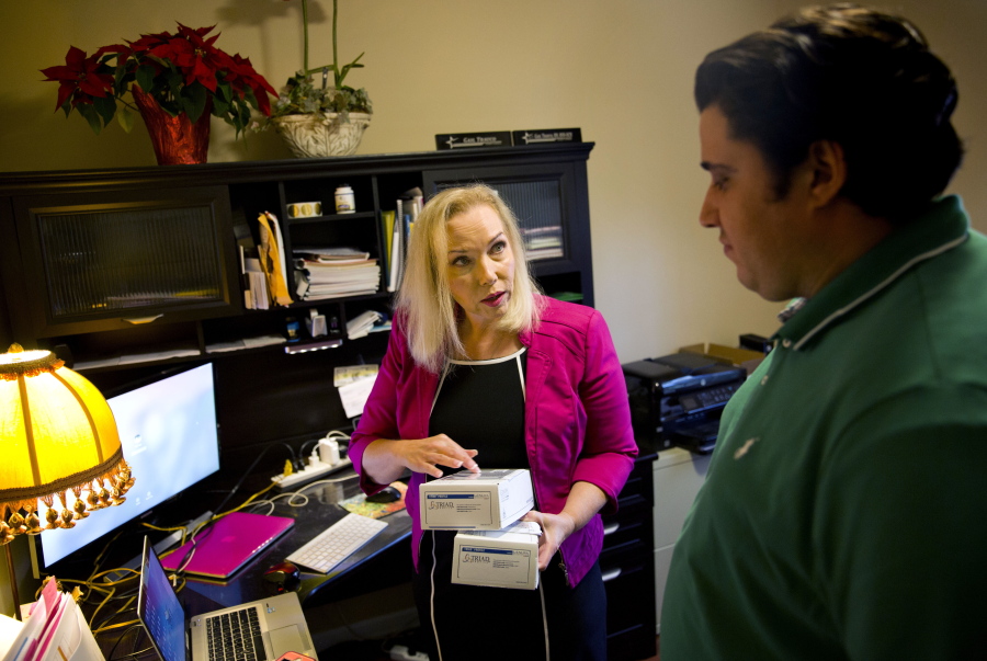 In this Monday, Dec. 4, 2017, photo, Gail Trauco, owner of The PharmaKon, left, talks with Jordan Rubio, her office manager and son, while working in her home office in Peachtree City, Ga. Trauco's insurer is eliminating her company's policy known as a preferred provider organization, or PPO, replacing it with a health maintenance organization, or HMO, a change that would limit the choice of doctors for her five employees. Her annual costs were scheduled to rise nearly $10,000 in 2018.