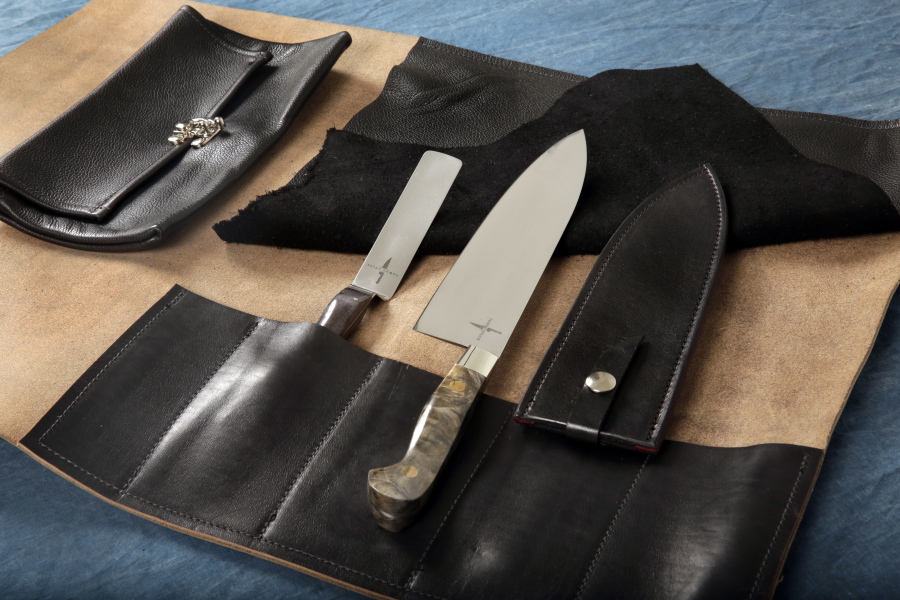 The Town Cutler Chef Kit, that consists of their Black Leather 5-Slot Knife Wrap, an 8.5-inch AEB-L Stainless Steel Chef Knife with Buckeye Burl Handle and leather scabbard, right, and a 4-inch Charcoal Palette Knife.