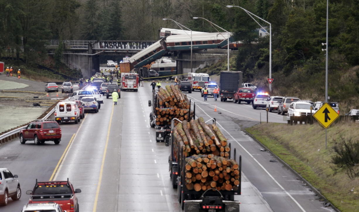 Logging trucks remain stopped just before where cars from an Amtrak train lay spilled onto Interstate 5 below alongside smashed vehicles as some train cars remain on the tracks above Monday, Dec. 18, 2017, in DuPont, Wash. The Amtrak train making the first-ever run along a faster new route hurtled off the overpass Monday near Tacoma and spilled some of its cars onto the highway below, killing some people, authorities said. Seventy-eight passengers and five crew members were aboard when the train moving at more than 80 mph derailed about 40 miles south of Seattle before 8 a.m., Amtrak said.