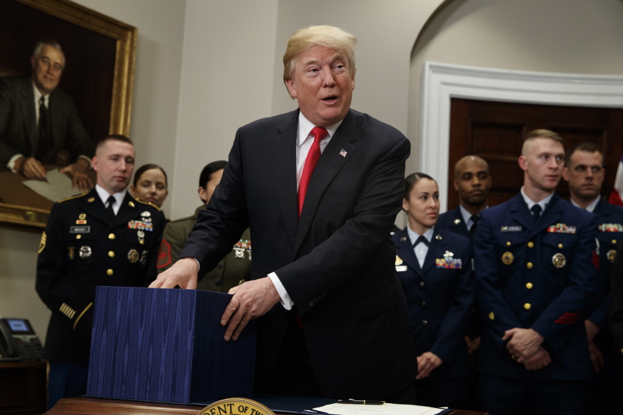 President Donald Trump holds onto a box containing the National Defense Authorization Act for Fiscal Year 2018 bill, in the Roosevelt Room of the White House, Tuesday in Washington.