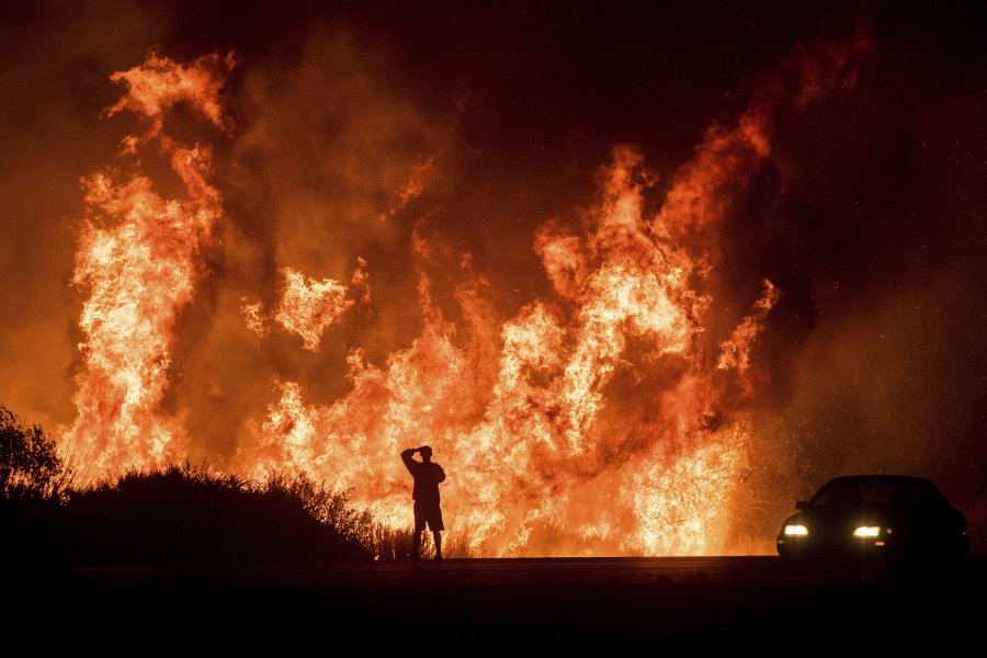 FILE - A motorist on Highway 101 watches flames from the Thomas fire leap above the roadway north of Ventura, Calif., on Wednesday, Dec. 6, 2017.