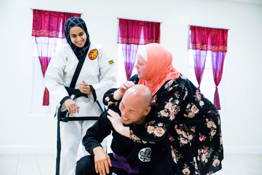 Fauzia Lala watches as Officer Craig Hanaumi of the Bellevue Police department helps Amelia Neighbors learn the technique used in choke holds during a self-defense seminar at the Muslim Association of Puget Sound, in Redmond, Wash., on Saturday, Dec. 23, 2017.