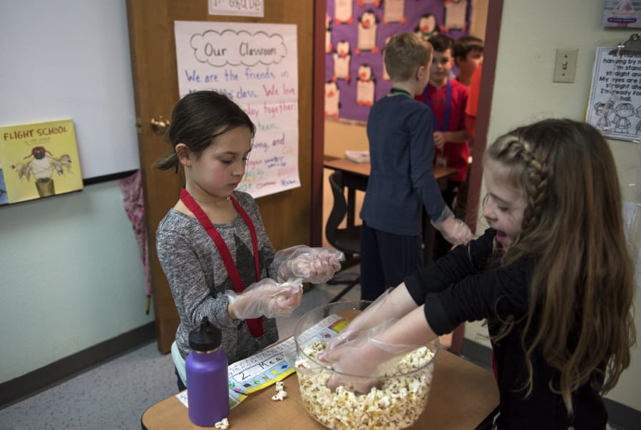 King’s Way Christian Schools first-graders Meah Carlson, left, and Cali Creagan, right, pack bags full of popcorn to sell Thursday during the marketplace section of the school’s new yearlong MicroSociety project. The curriculum puts students in charge of running a country over the course of the year.