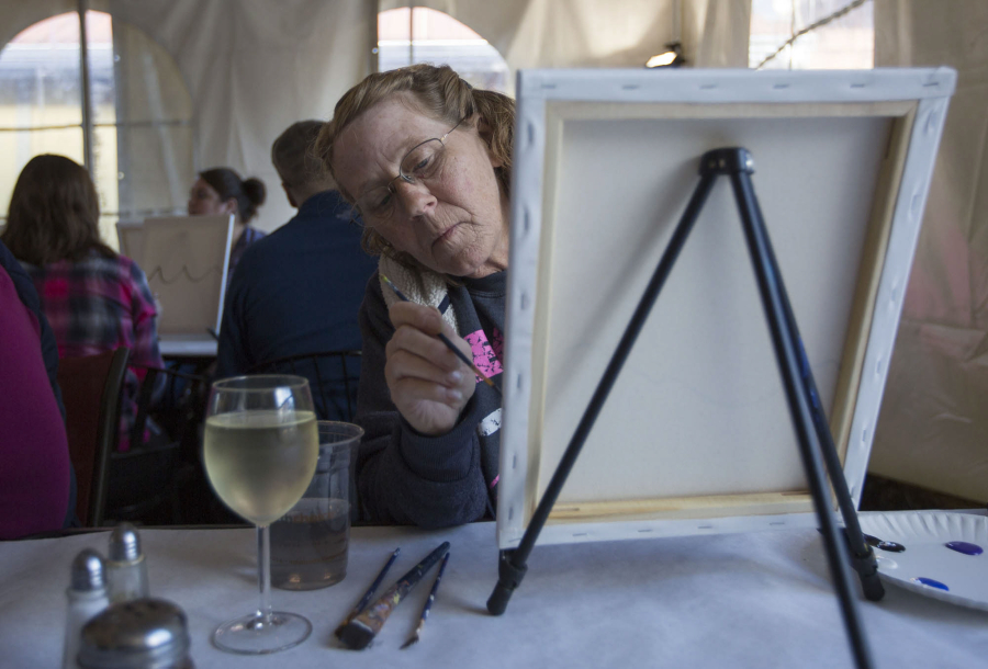 A painter paints with a glass of white wine nearby as she attends a guided painting lesson at the Rusty Grape Vineyard in Battle Ground Sunday.