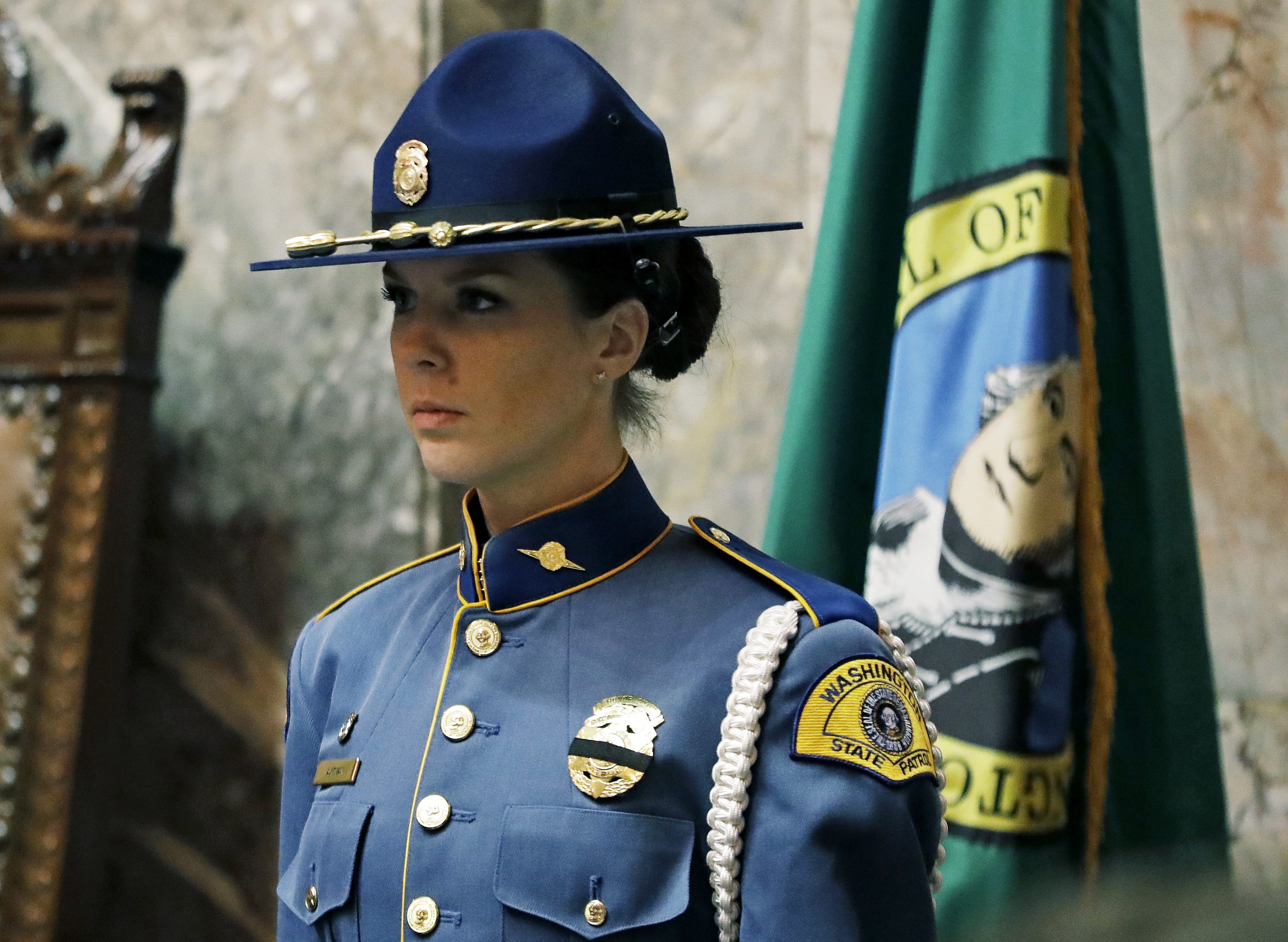 A Washington State Patrol trooper wears a black band across her badge, Monday, Jan. 8, 2018 to honor Pierce County Sheriff's Deputy Daniel McCartney, who was shot during a foot chase late Sunday night as he responded to a home invasion in Frederickson, Wash., and who died of his wounds later that night. The trooper was taking part in an honor guard ceremony Monday to open the first day of the 2018 legislative session. (AP Photo/Ted S.