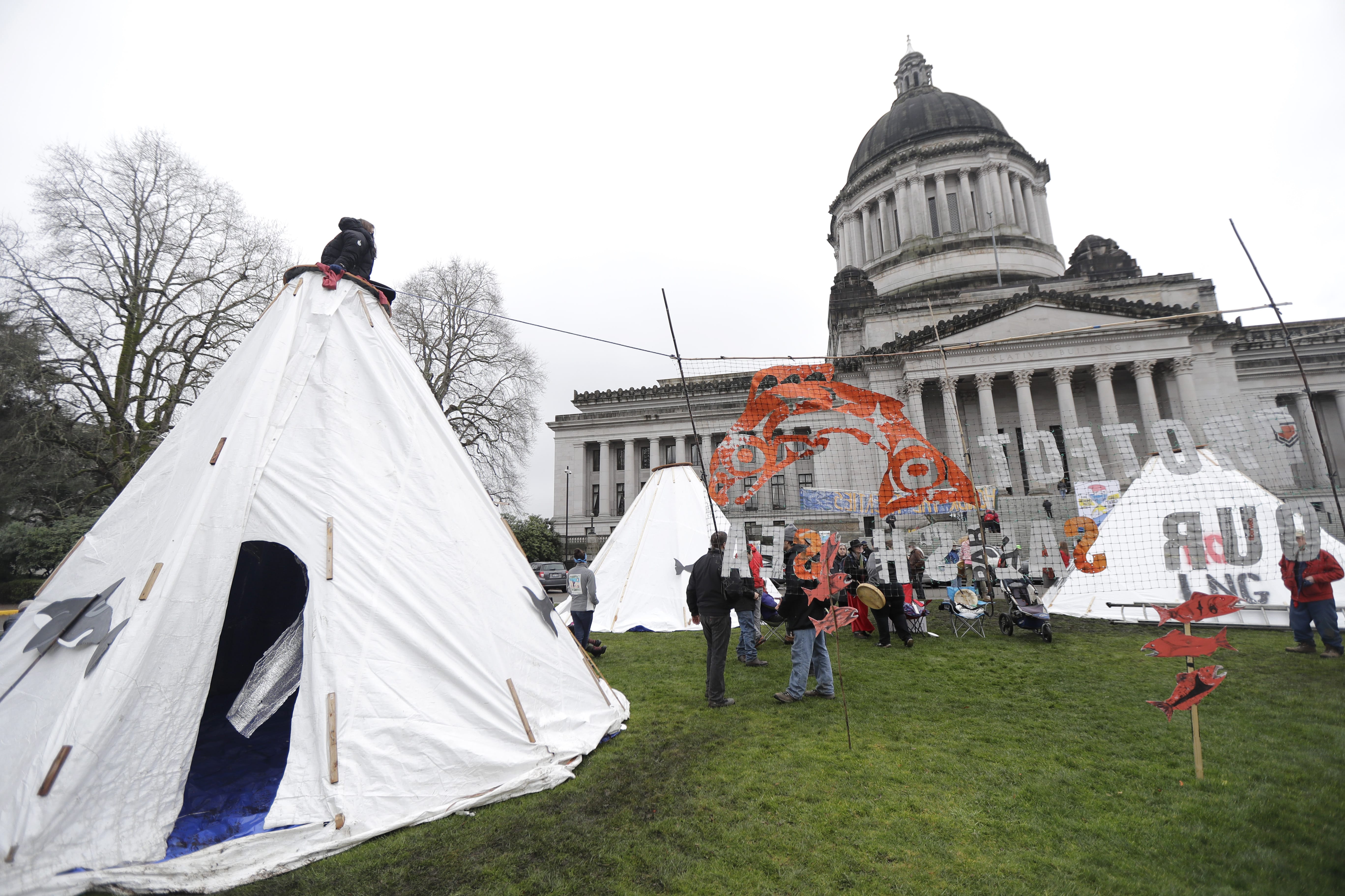 Activists gather around structures erected on a grassy area in front of the Legislative building at the Capitol in Olympia, Wash., Monday, Jan. 8, 2018, the first day of the 2018 legislative session. The structures were part of a day of demonstrations by several groups from across the state supporting climate-change and environmental issues. (AP Photo/Ted S.