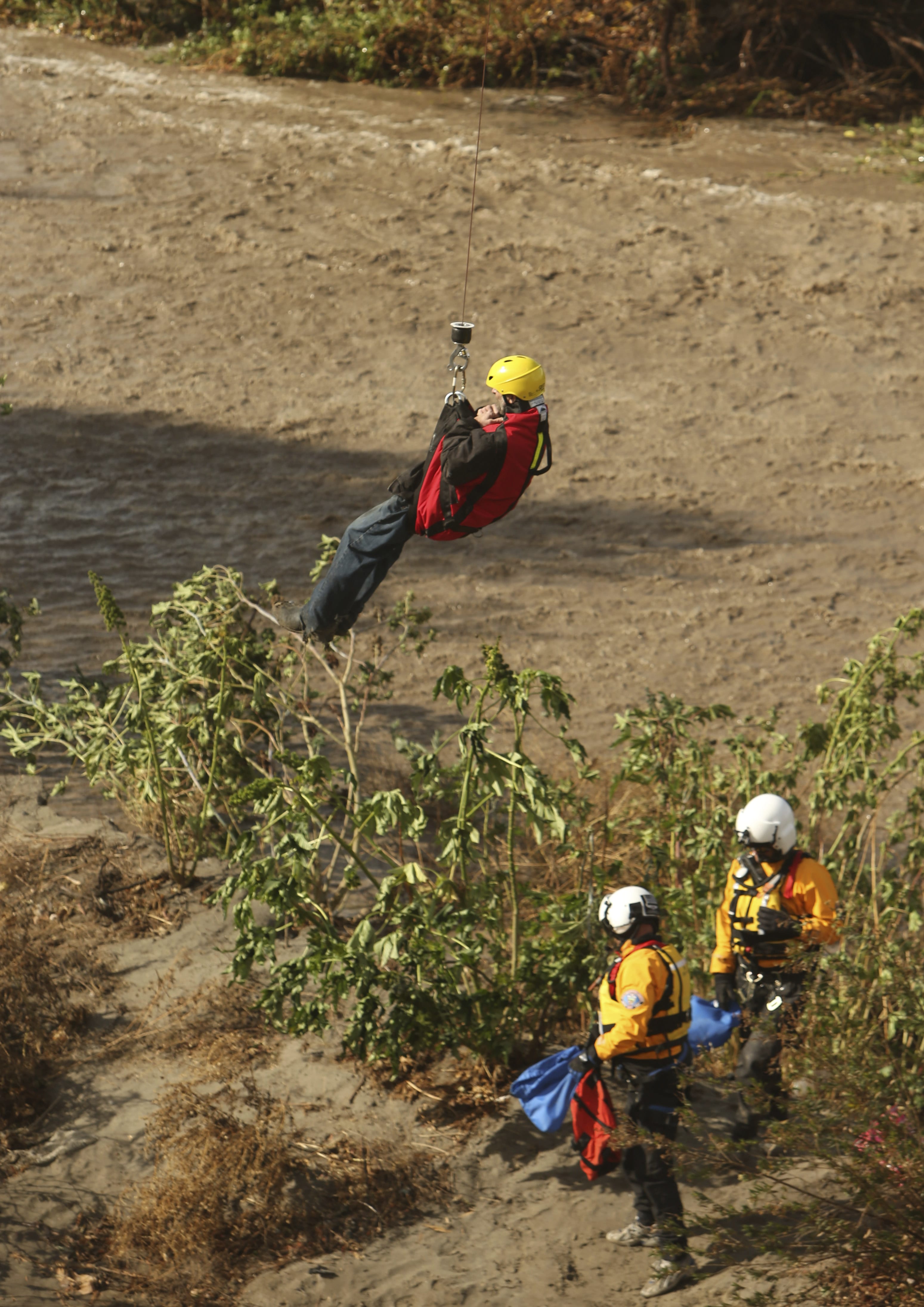 A man is hoisted out with the help of a San Bernardino County Sheriff's helicopter on Tuesday, Jan. 9, 2018, in the Santa Ana River and near the borders of Rialto, Colton, and Riverside, Calif. Three people and a dog were rescued by a helicopter after large amounts of rain fell, trapping the group at a homeless encampment in the river.