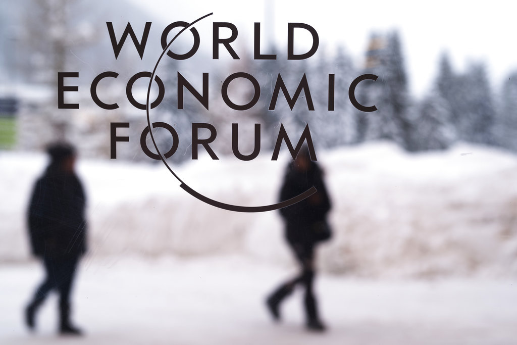 Two persons walk behind the logo of the World Economic Forum at the meeting's conference center in Davos, Switzerland, Sunday, Jan. 21, 2018. One question looms as President Donald Trump packs his bags and heads for the mountains of Switzerland later this week: How will the diet Coke-loving nationalist fit in with the champagne-swilling globalists he’ll encounter at the World Economic Forum in Davos?