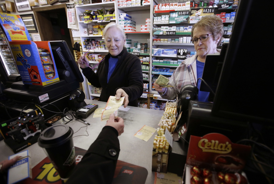 Cashiers Kathy Robinson, left, and Ethel Kroska, right, both of Merrimack, N.H., sell a lottery ticket Sunday, Jan. 7, 2018, to Diane Ackley, hand only below, at Reeds Ferry Market convenience store, in Merrimack. A lone Powerball ticket sold at Reeds Ferry Market matched all six numbers and will claim a $570 million jackpot, one day after another single ticket sold in Florida nabbed a $450 million Mega Millions grand prize.