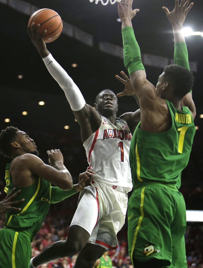 Arizona guard Rawle Alkins (1) drives between Oregon forward Troy Brown and Kenny Wooten (1) in the second half during an NCAA college basketball game, Saturday, Jan. 13, 2018, in Tucson, Ariz.
