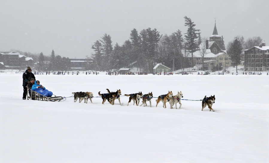 John Houghton, of Vermontville, N.Y., and his sled dog team, give a ride to a couple Jan. 30, 2015, in a snowfall, around Mirror Lake in Lake Placid, N.Y.