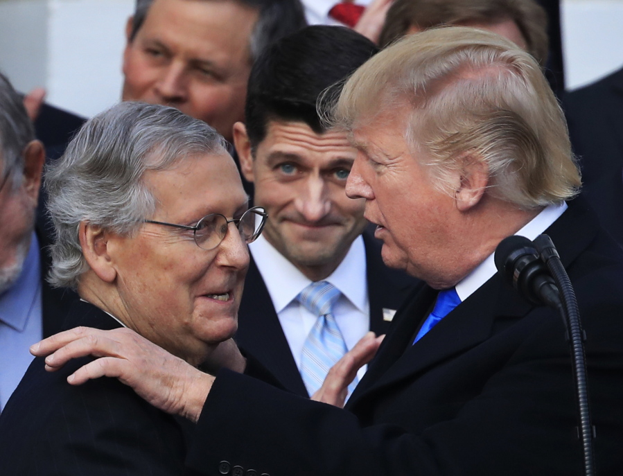 President Donald Trump congratulates Senate Majority Leader Mitch McConnell of Kentucky while House Speaker Paul Ryan of Wisconsin watches to acknowledge the final passage of tax overhaul legislation by Congress on Dec. 20, 2017, at the White House in Washington.